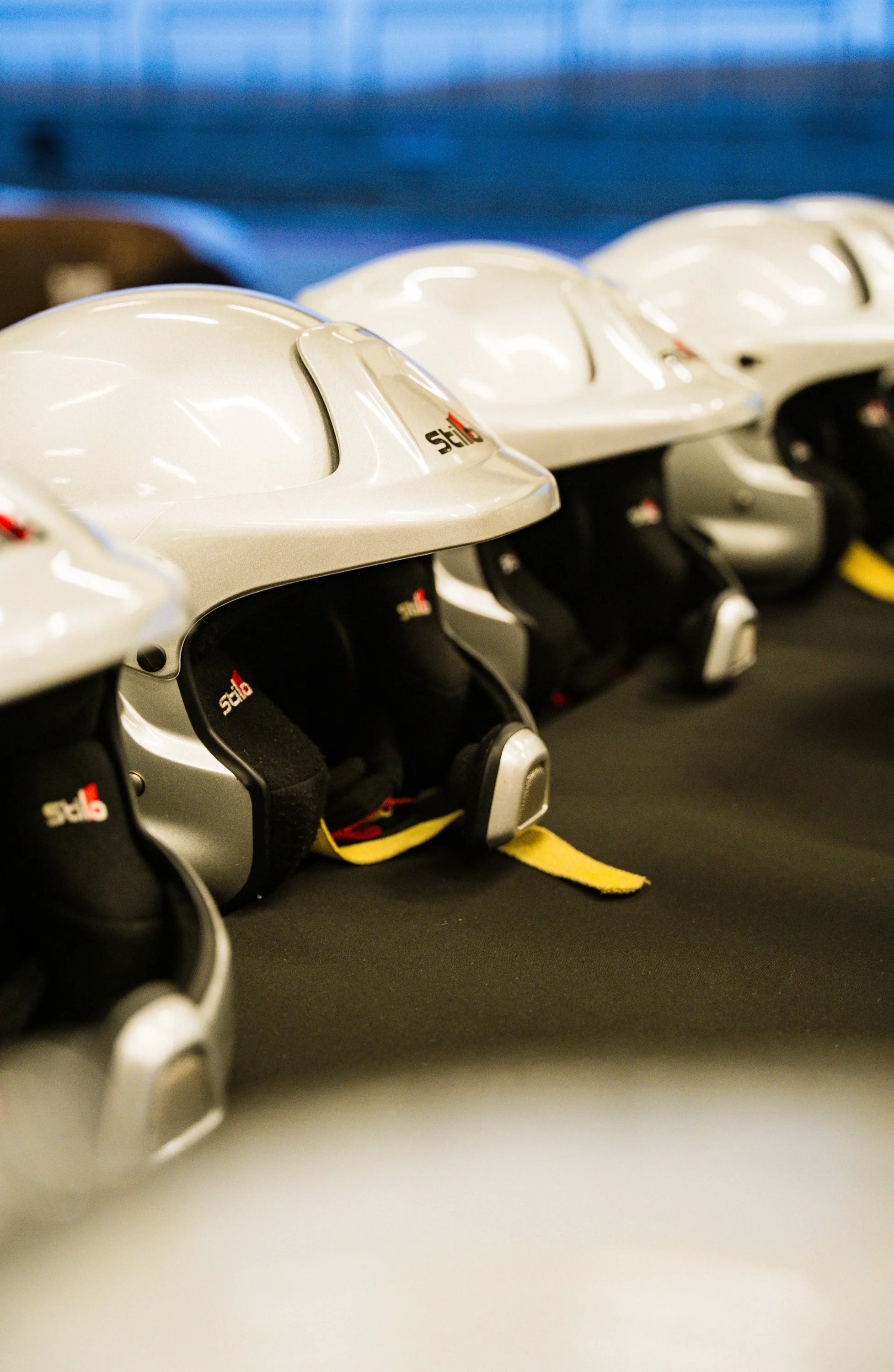 Row of white hockey helmets with black and yellow interior padding, resting on a black surface.