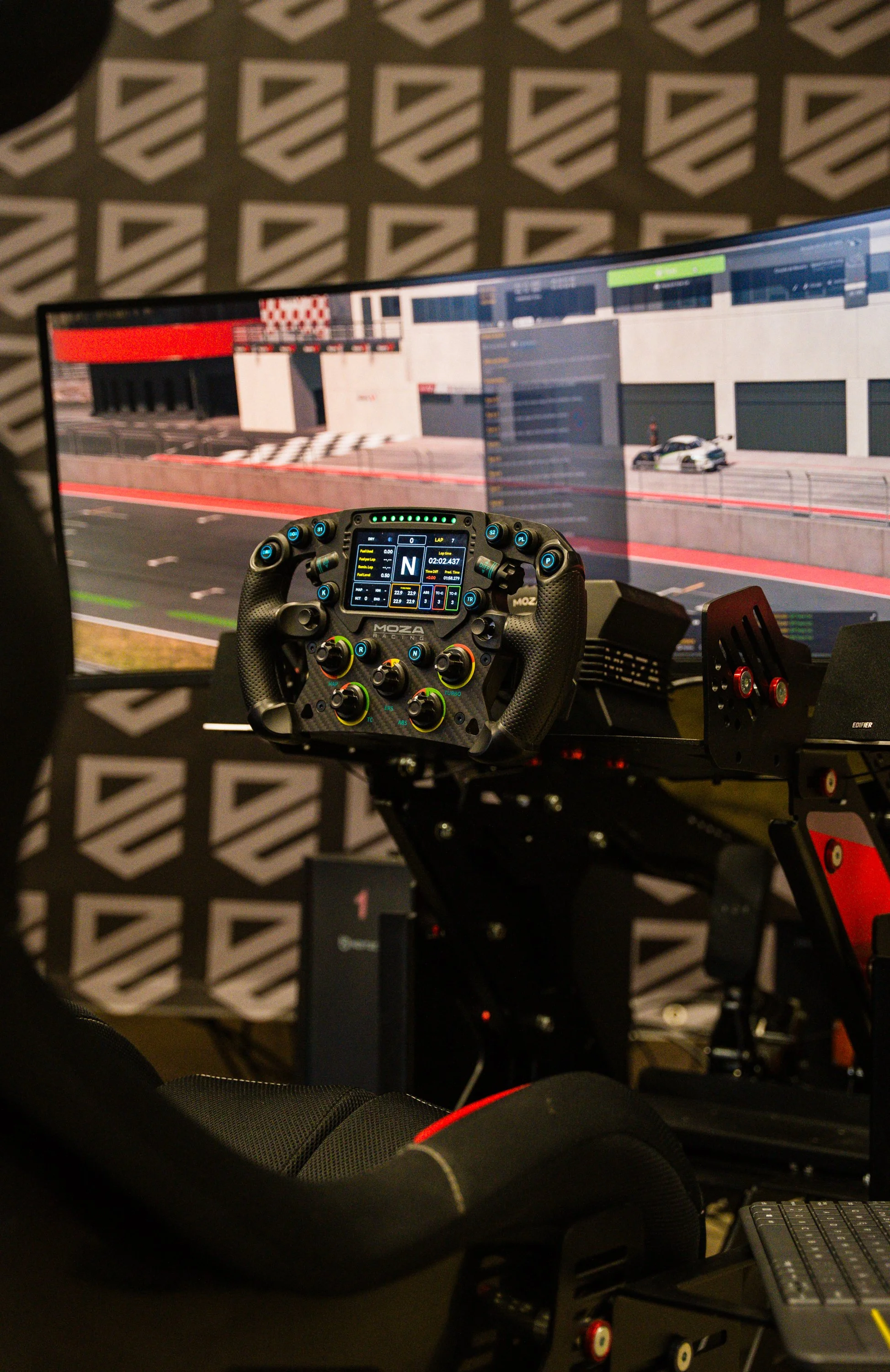 A racing simulation setup with a monitor displaying a race track, a racing wheel controller, and a keyboard, all arranged in a dedicated racing gaming environment.