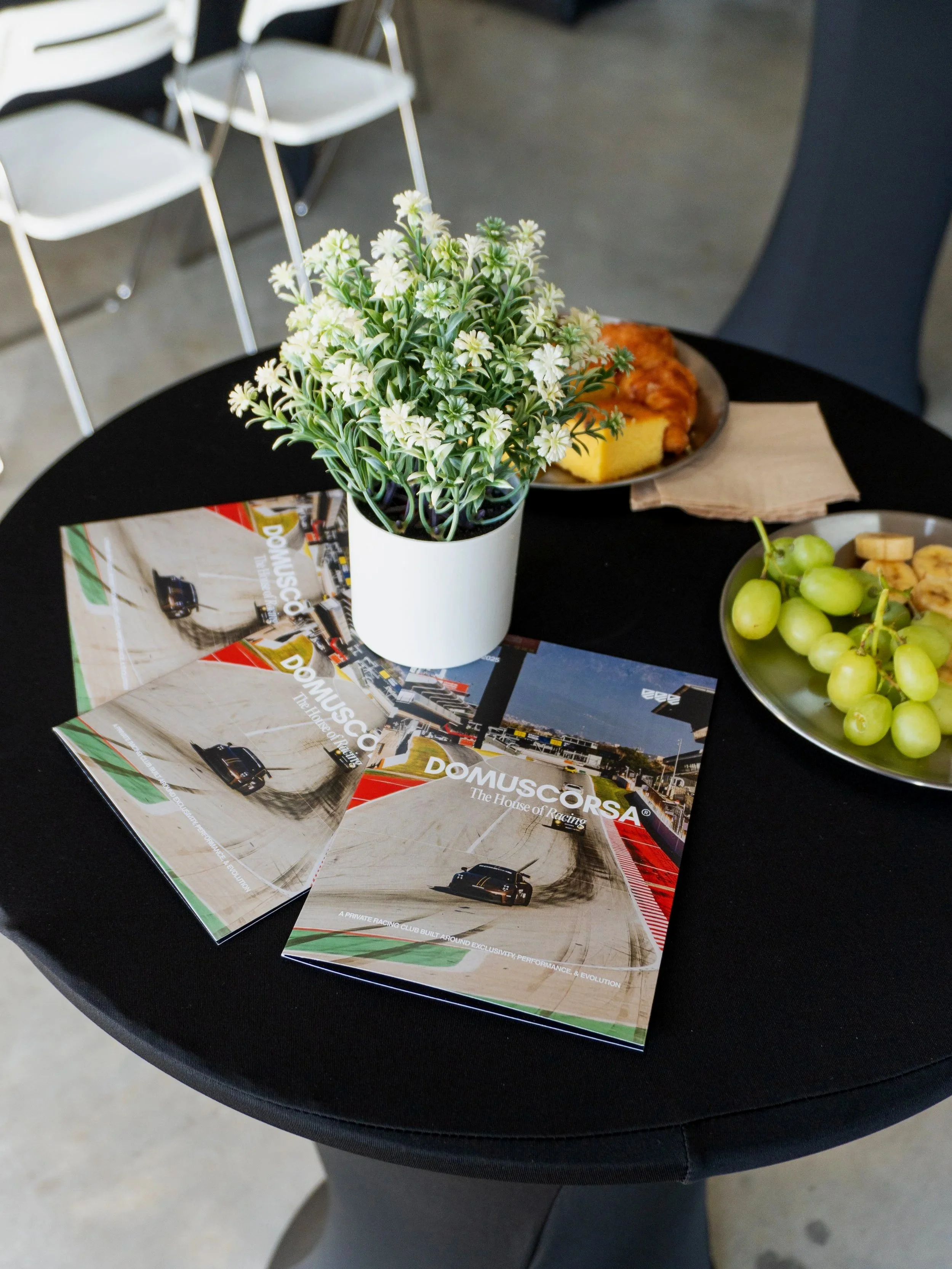 Three pamphlets for DomusCorsa, a racing club, are placed on a round black table.