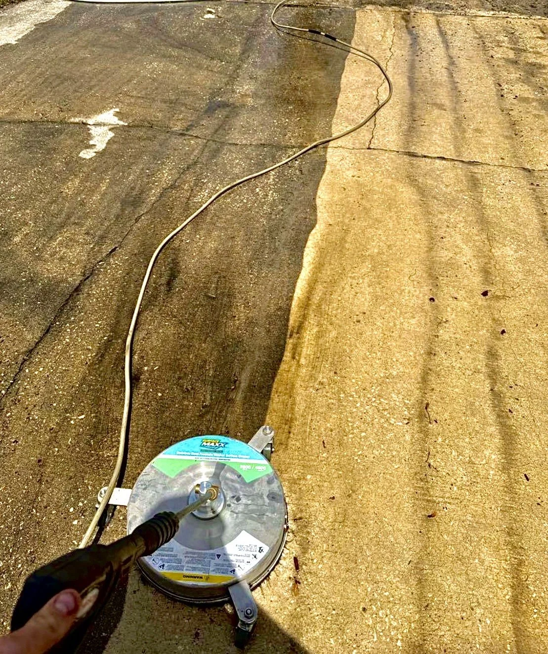 Person using a handheld power tool to cut or grind concrete pavement on a paved surface.