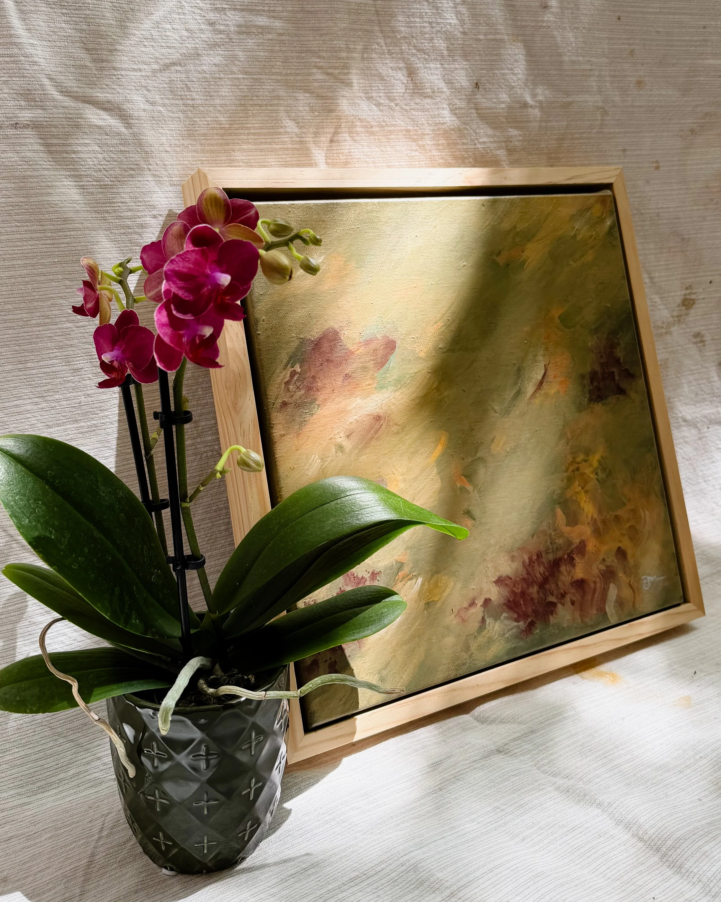 Potted pink orchids near a framed abstract painting on a neutral canvas surface.
