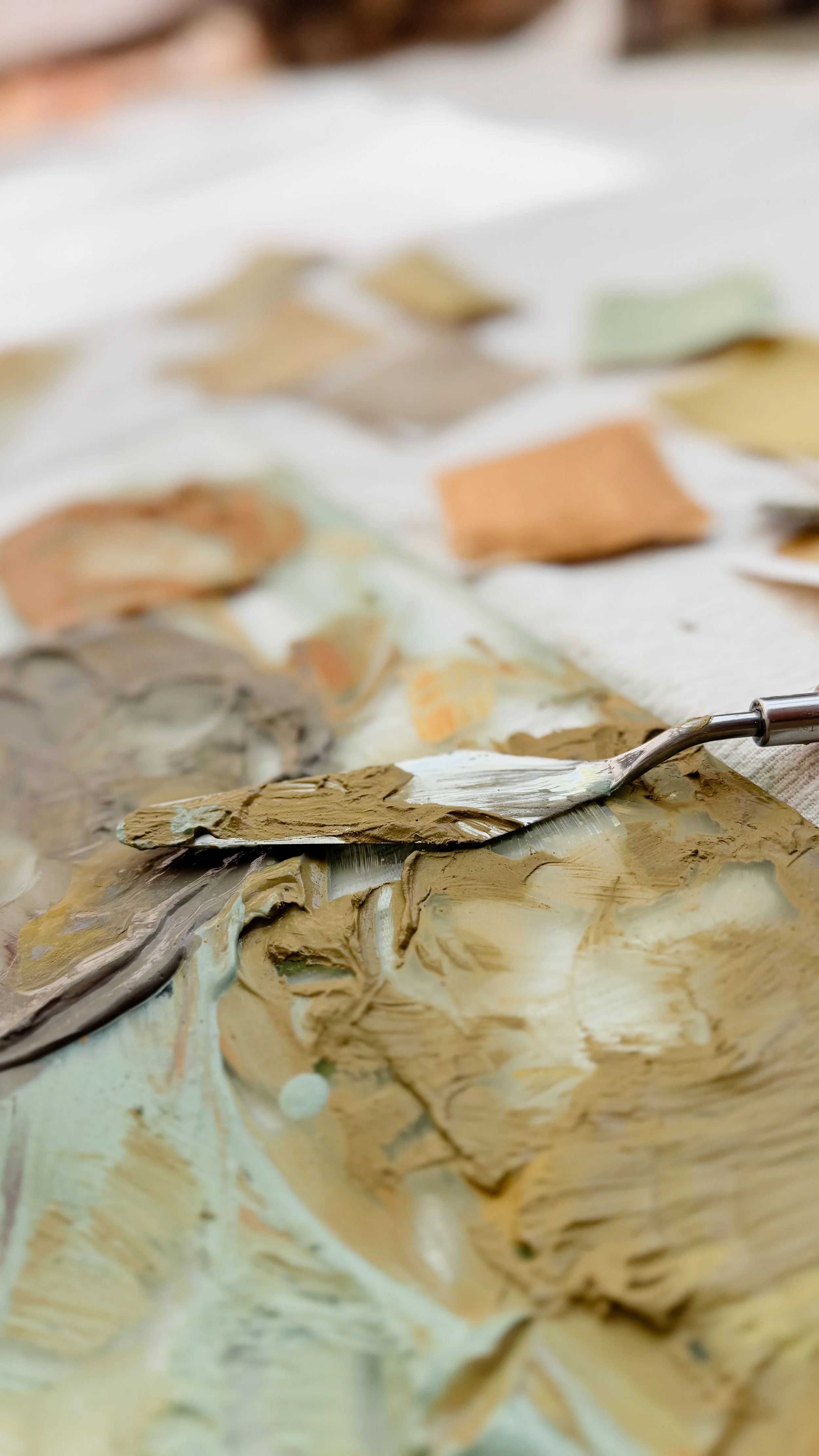 Close-up of various shades and textures of paint, with a metal spatula resting on a palette of mixing paints.