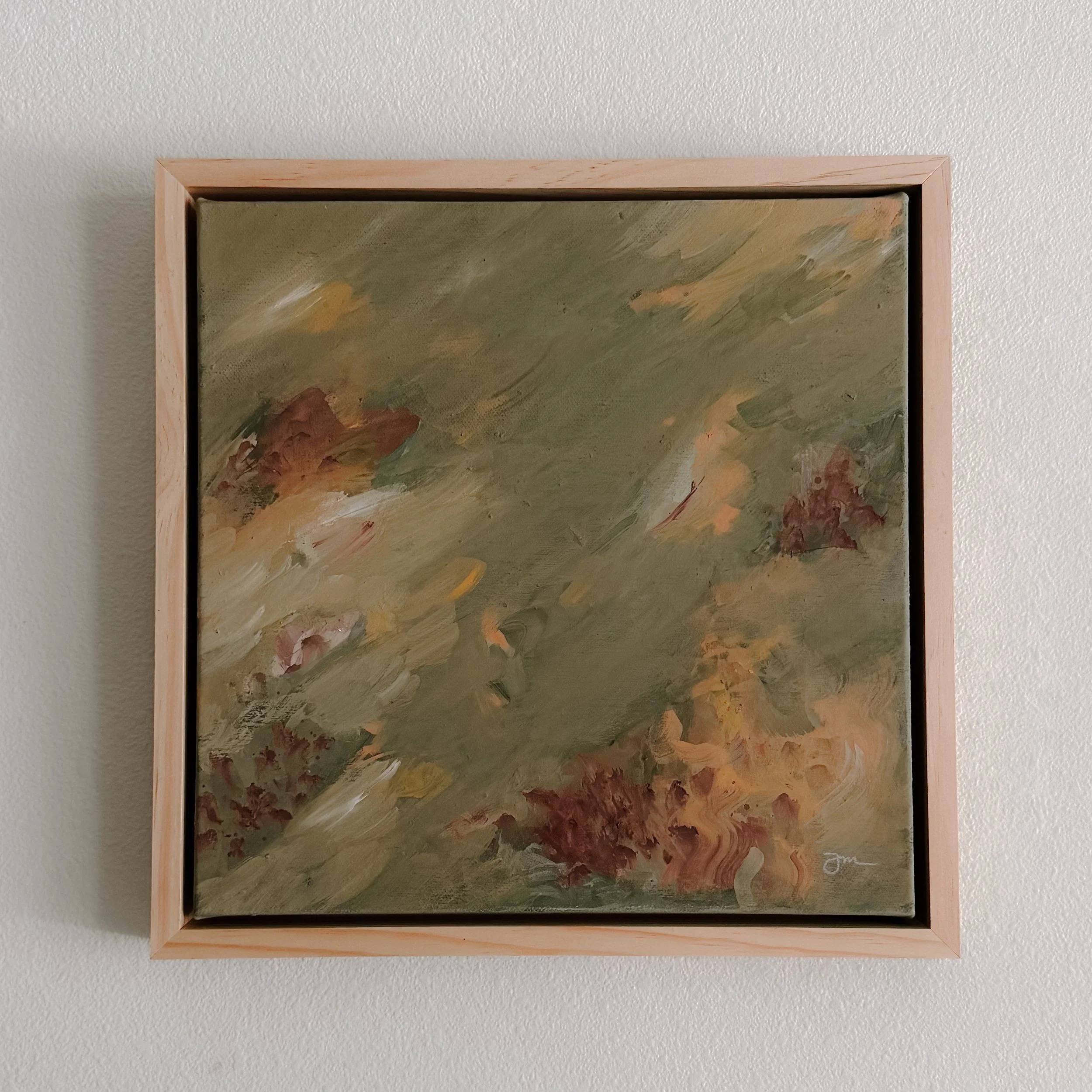 An abstract painting with muted earth tones framed in light wood, hanging on a white textured wall.
