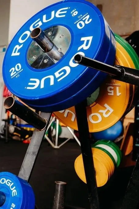 Stacked colorful weight plates on a rack at a gym, with blue, yellow, and green weights visible.