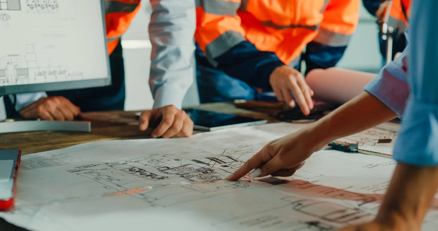 Group of engineers in safety vests examining architectural blueprints on a large table.