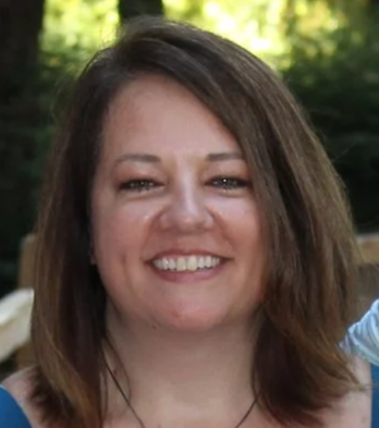 Katie Paulson smiling with shoulder-length brown hair, outdoors in a sunny environment.