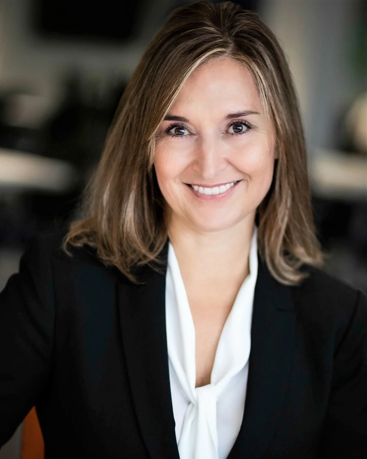 Professional woman with shoulder-length brown hair smiling in a business suit with a white blouse.