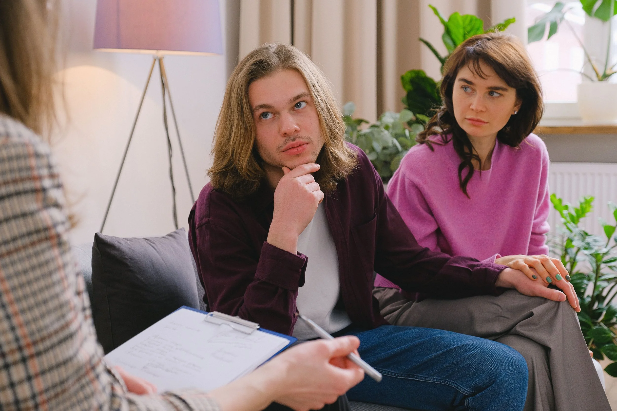 Two women and a man sitting on a couch having a conversation, with a woman holding a notepad and pen in the foreground.