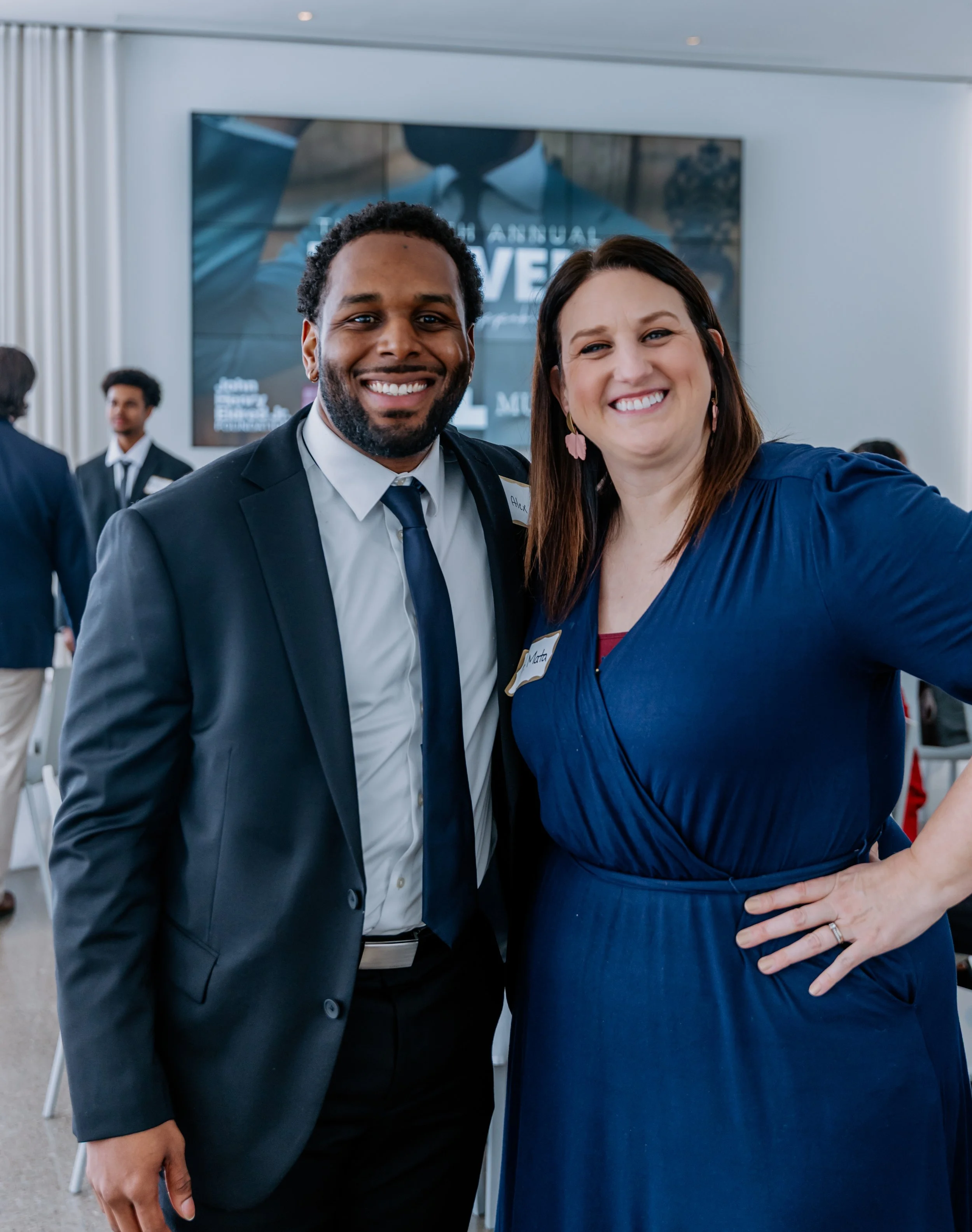 Dr. Alex Long and Dr. Andrea Mata taking a selfie at a formal event. The man is wearing a dark suit with a white shirt and a tie.
