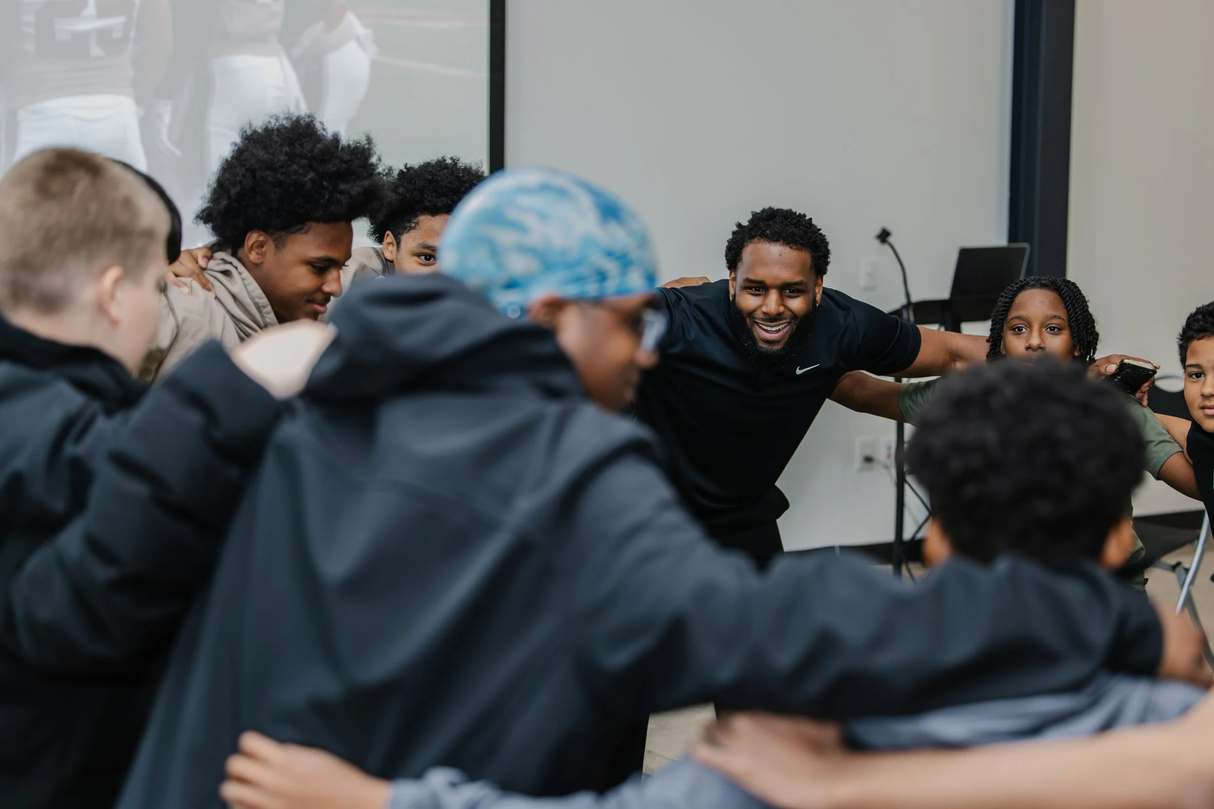 Group of diverse children and an adult smiling and gathered in a circle, engaging in a group activity in a classroom.