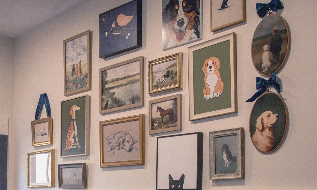 A wall decorated with various framed pictures and paintings, mostly of dogs and other animals, arranged in a gallery style.