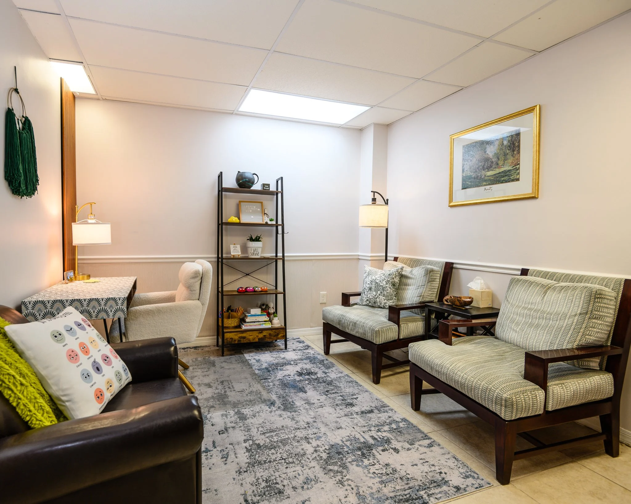 A cozy waiting room with multiple chairs, a bookshelf with decorative items, artwork on the walls, and a patterned rug on the floor.