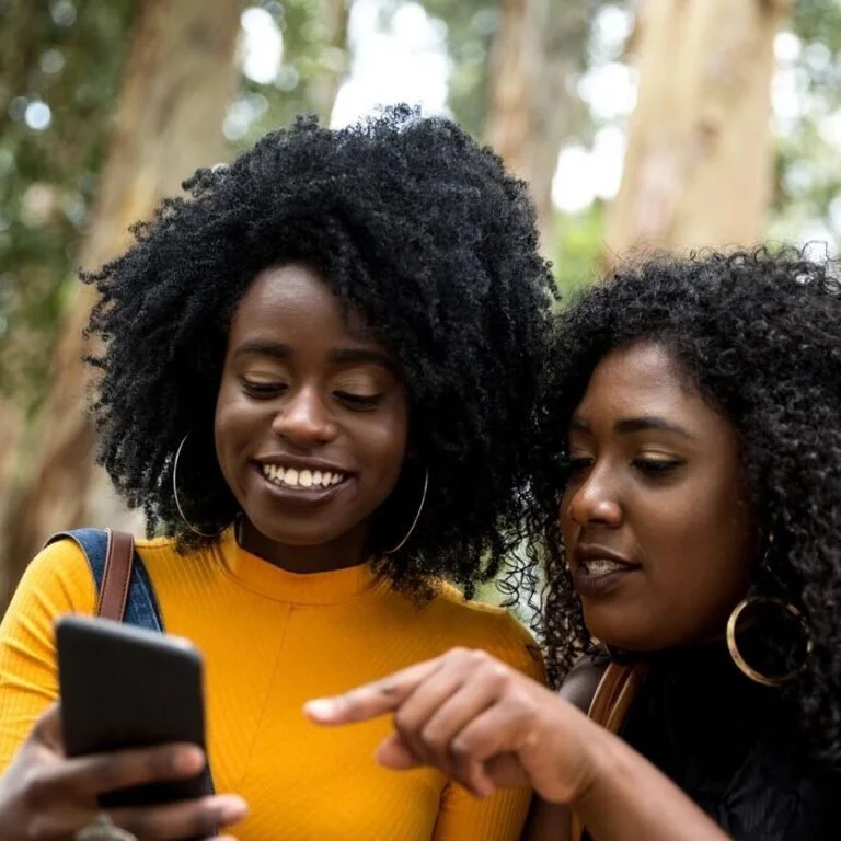Two women smiling with one woman pointing to the phone