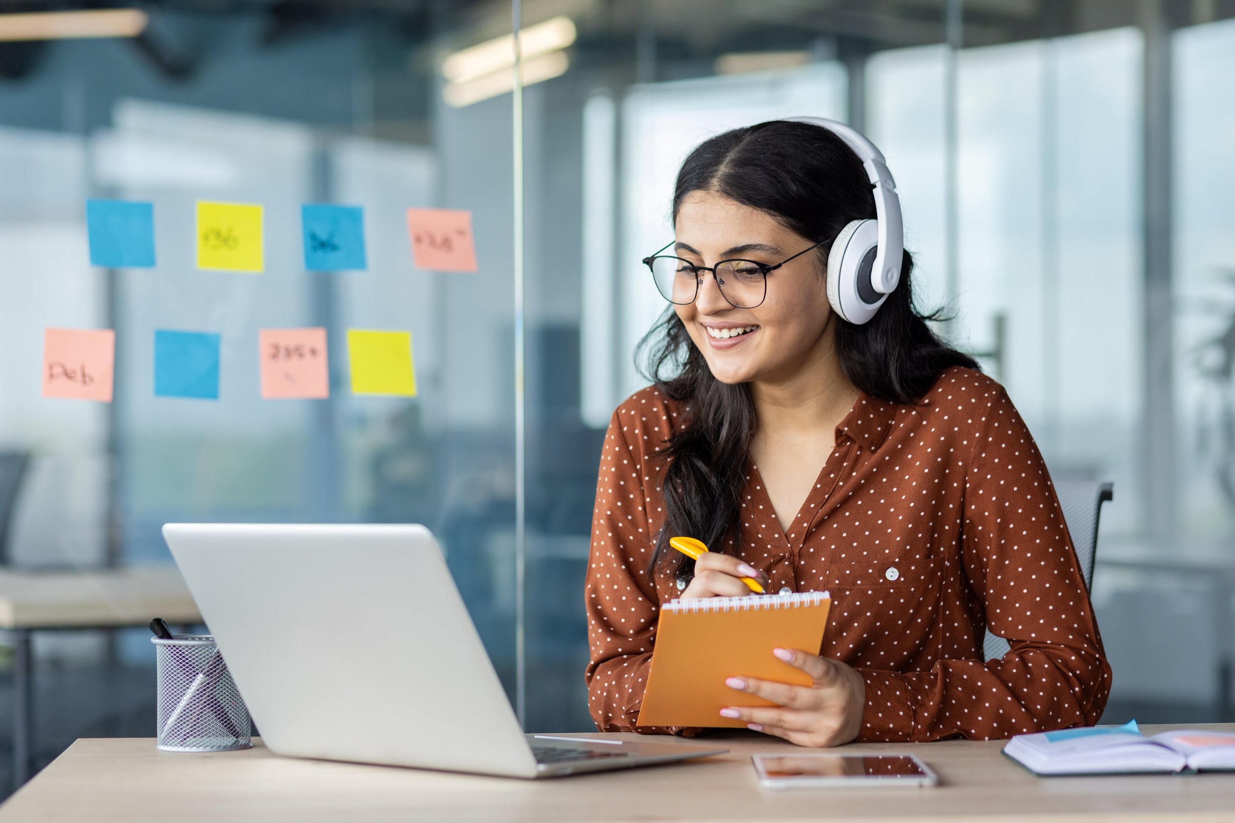 A female student making notes with headphones and her laptop