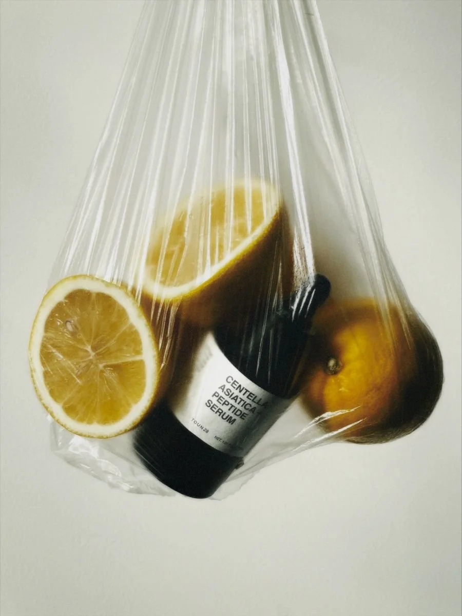 A plastic bag containing a bottle of serum labeled 'Centella Asiatica Peptide Serum' and several lemons.