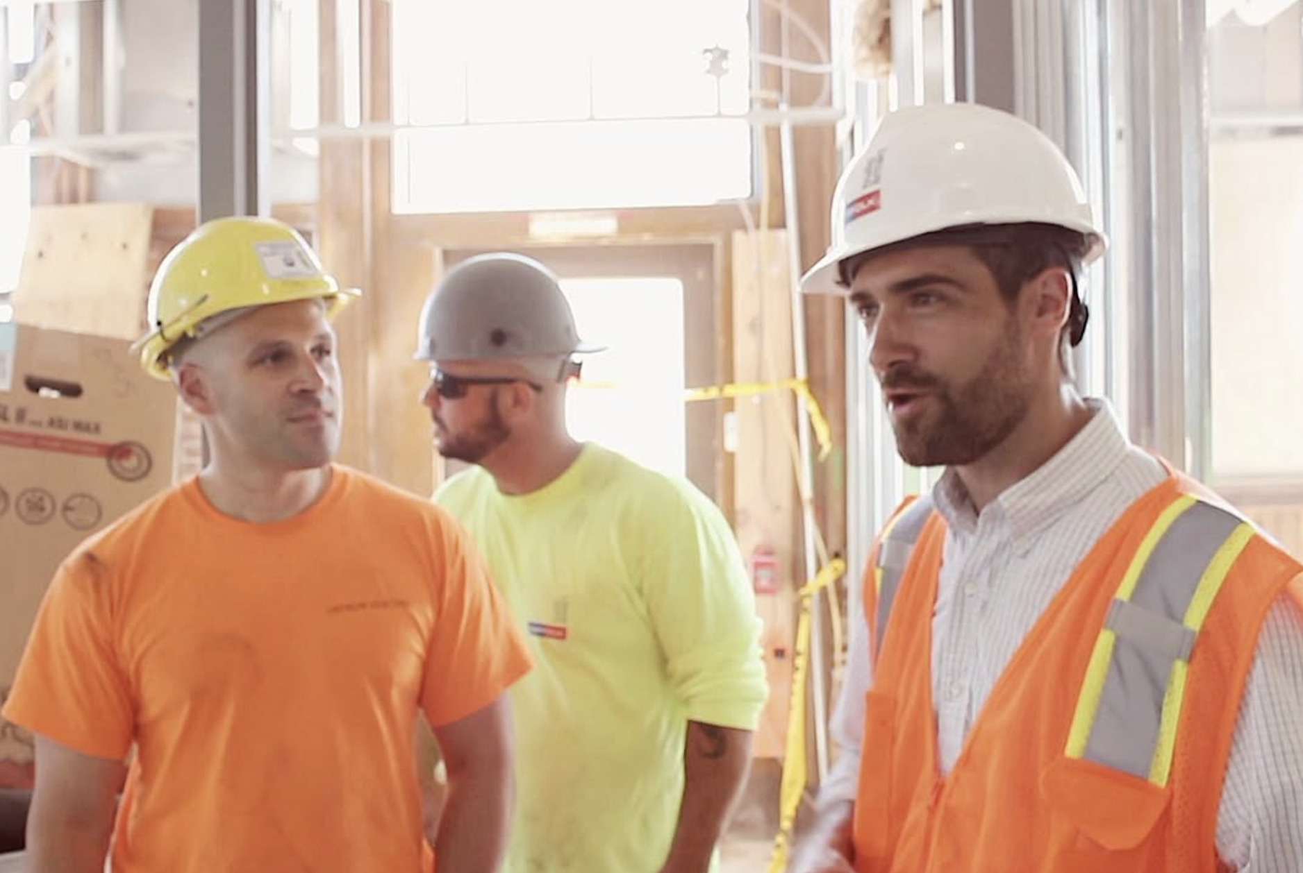 Three construction workers wearing safety helmets and high-visibility vests inside a building under construction.