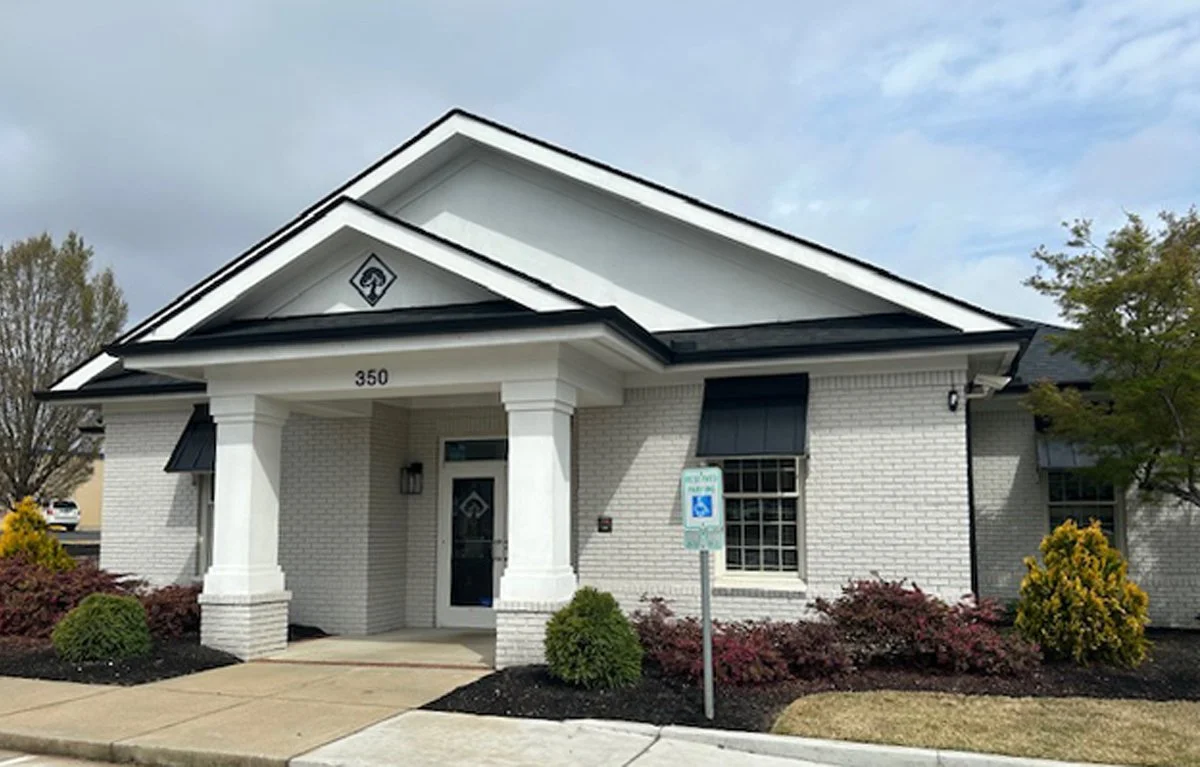 White brick building at address 350 with a dark roof and a covered entryway supported by two white columns. A tree logo is visible on the front gable.
