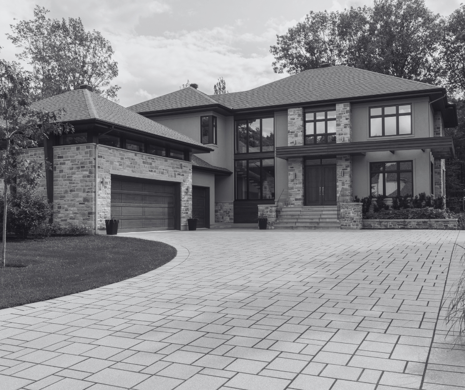 A large modern two-story house with a stone and stucco exterior, a double garage, and a paved driveway. The house features multiple large windows and a front entrance with steps leading up to double doors.