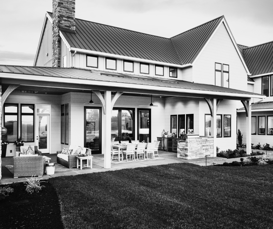 Black and white photo of a modern houses exterior with a covered patio, outdoor furniture, and a well-maintained lawn.