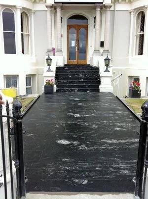 Flooded black pathway leading to the entrance of a white building with pillars and glass double doors.