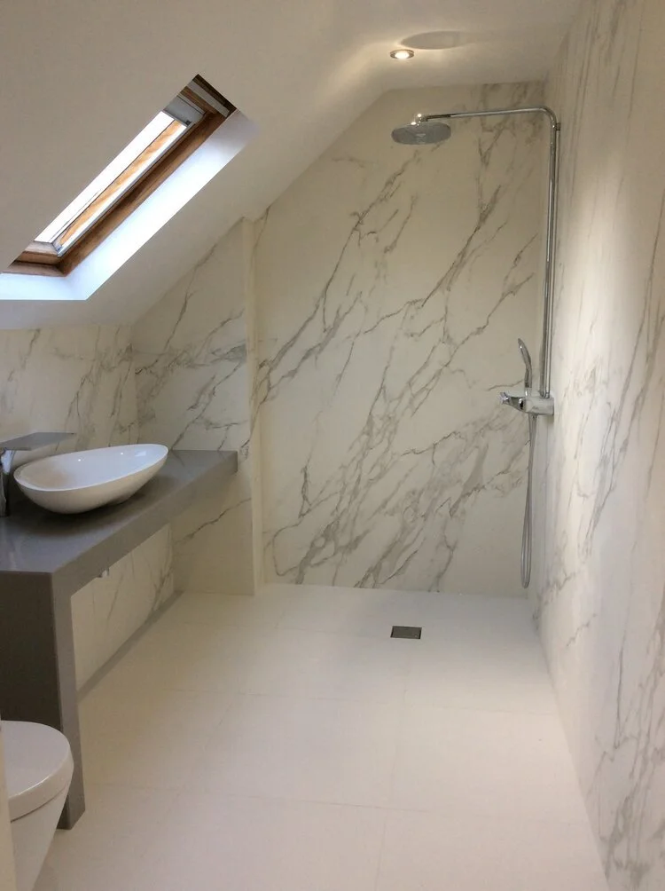 Modern bathroom with a skylight near the shower area, marble walls, a handheld showerhead, a vessel sink on a gray countertop, and a toilet.