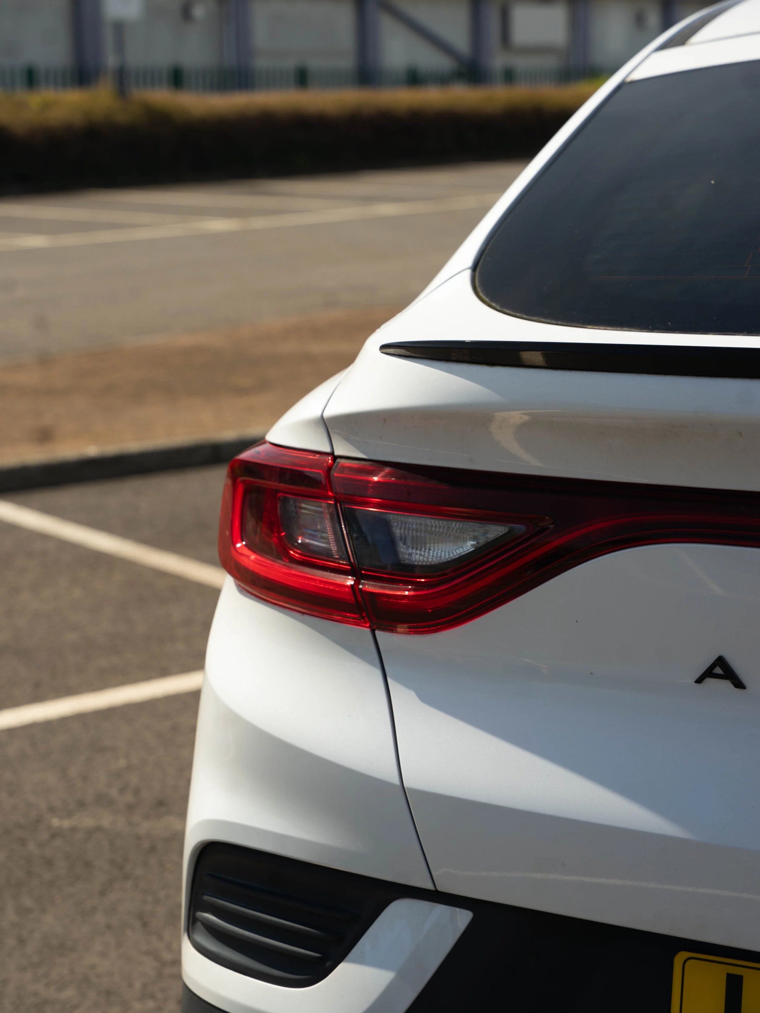 Close-up of the rear of a white Renault Arkana parked in an outdoor parking lot, showing tail light, rear window, and rear bumper.