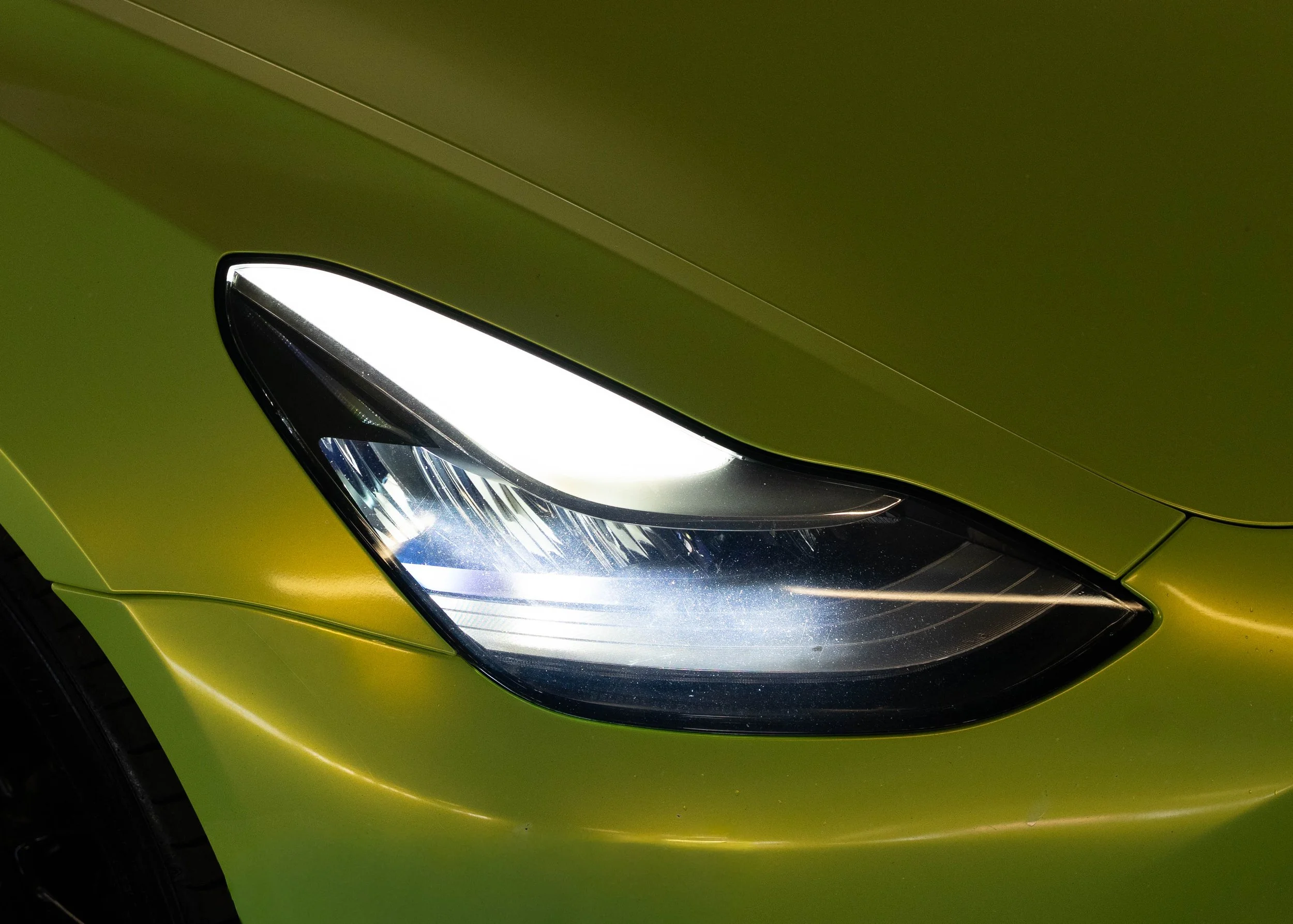 Close-up of the front left corner of a green Tesla Model Y, showing its headlight and part of the hood.