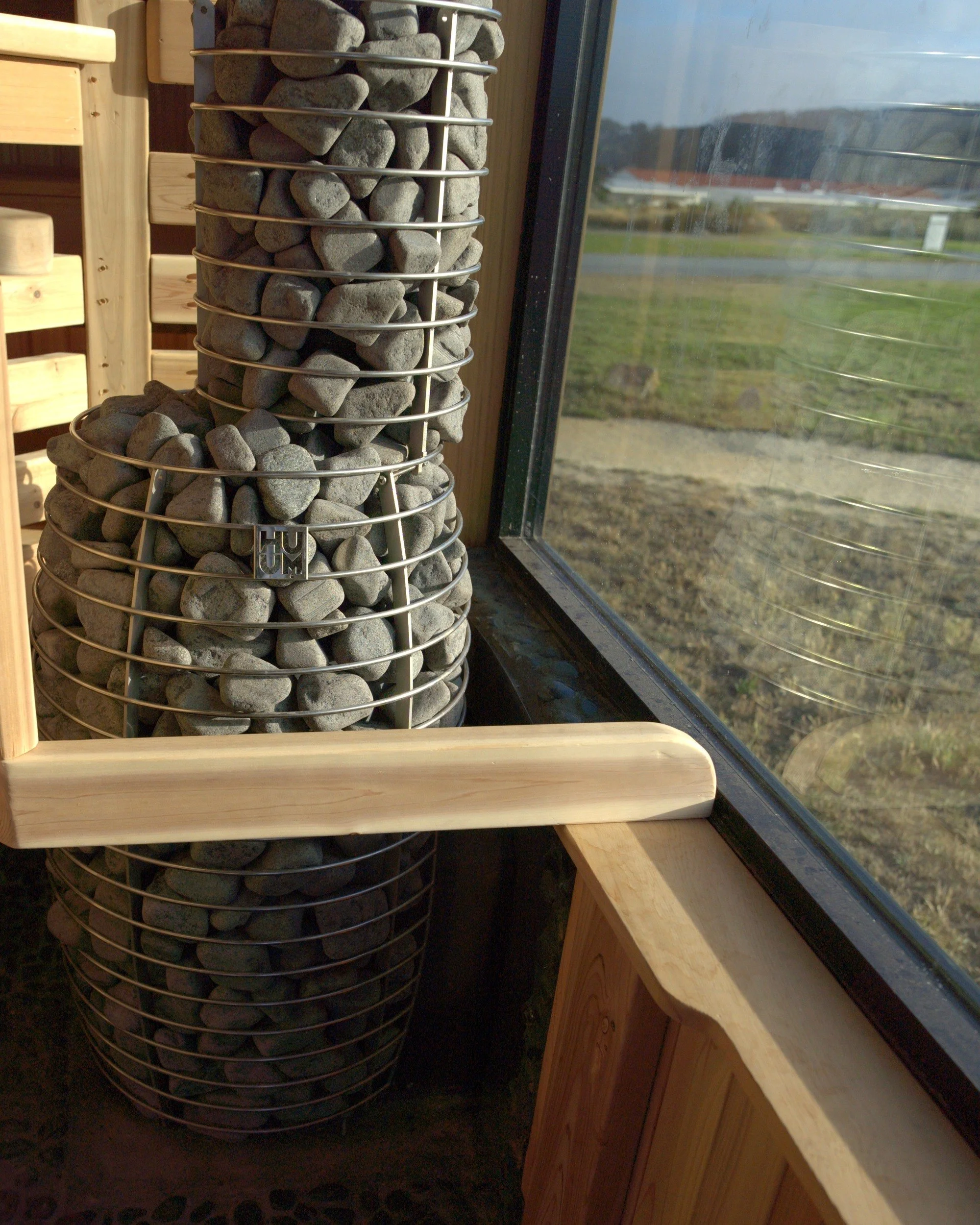 Stone-filled sauna heater framed by warm cedar benches and a window.