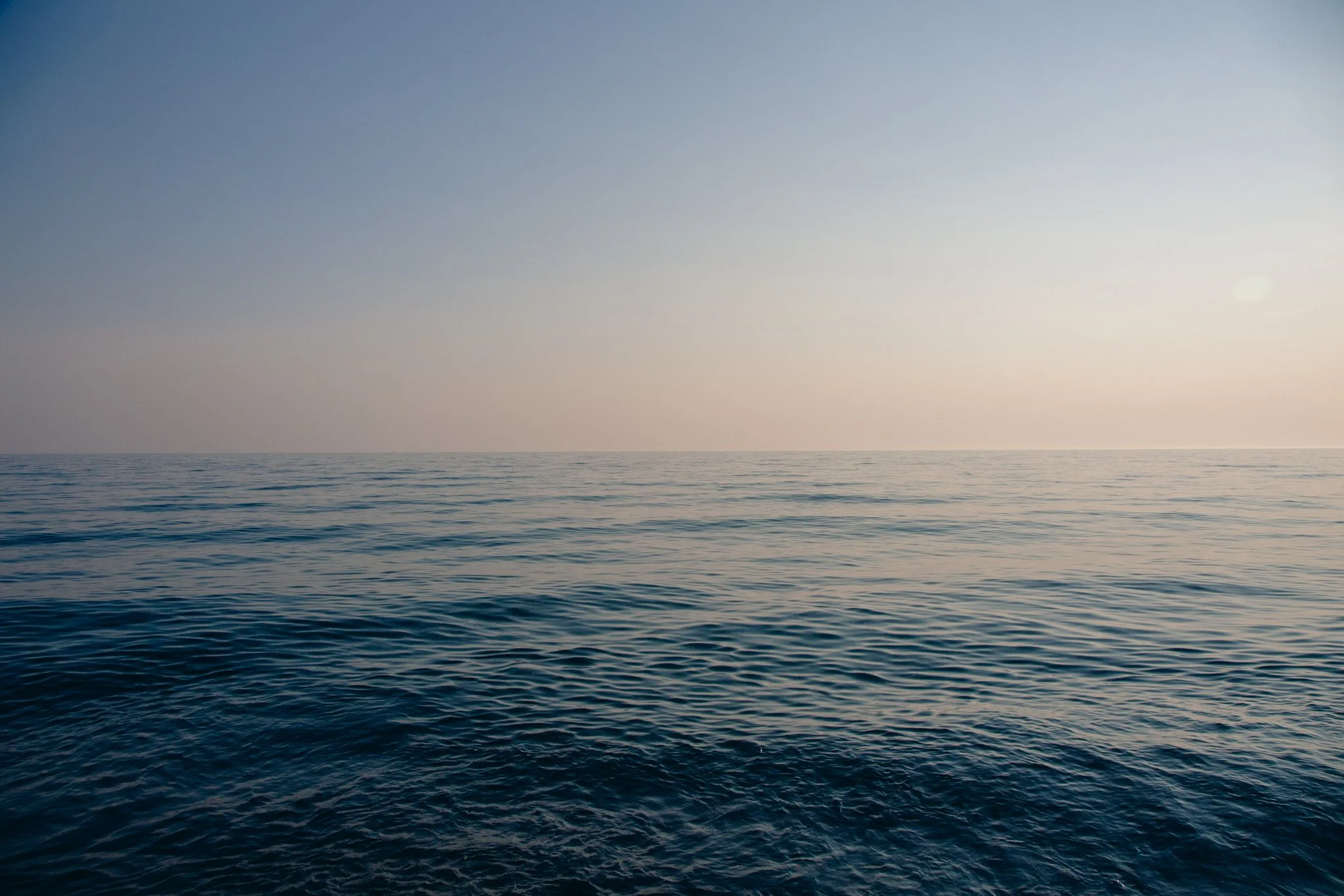 A vast ocean with gentle waves, under a clear sky with the sun near the horizon.