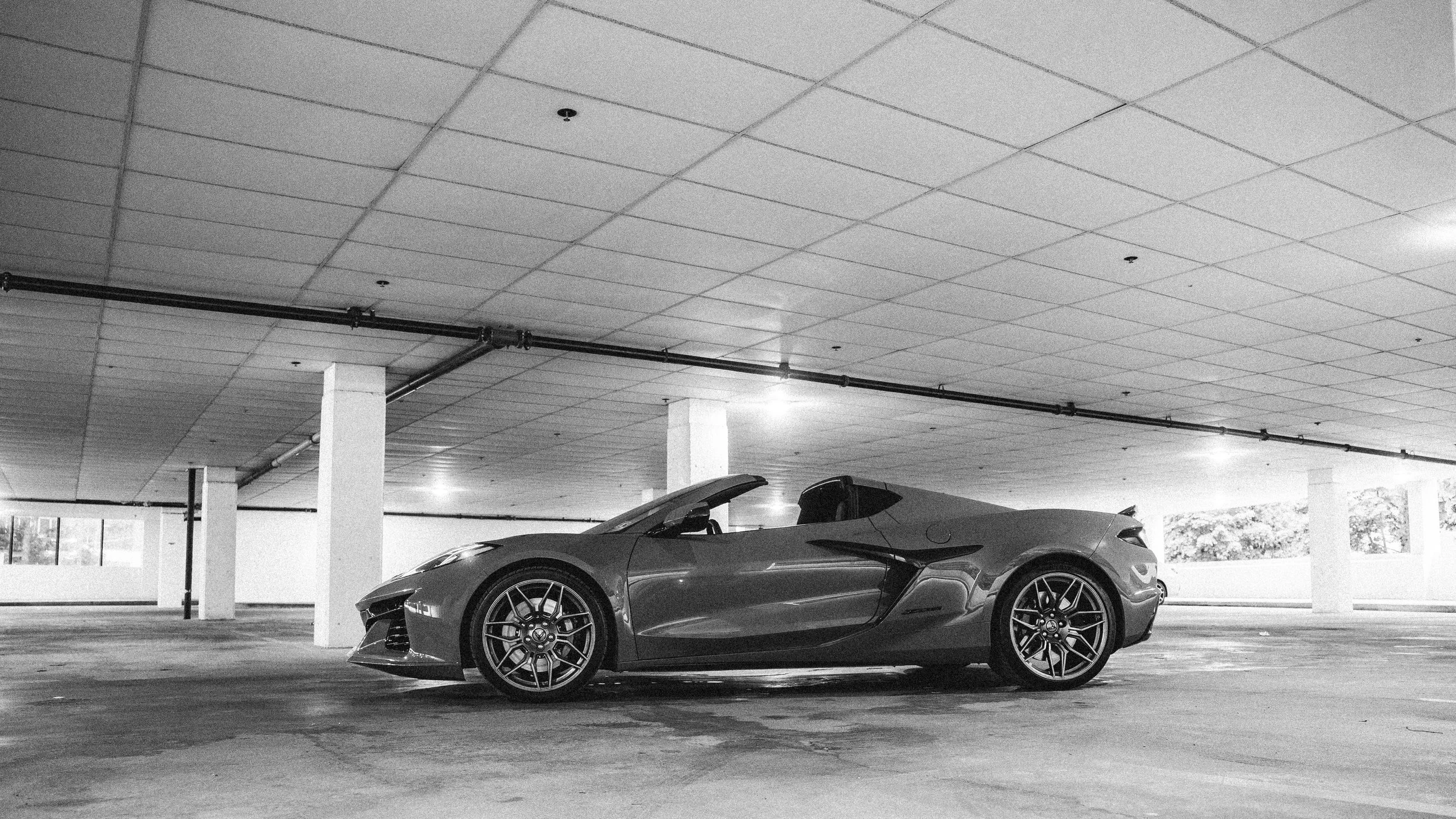 A sleek sports car parked in an underground parking garage with a low ceiling and supporting columns.