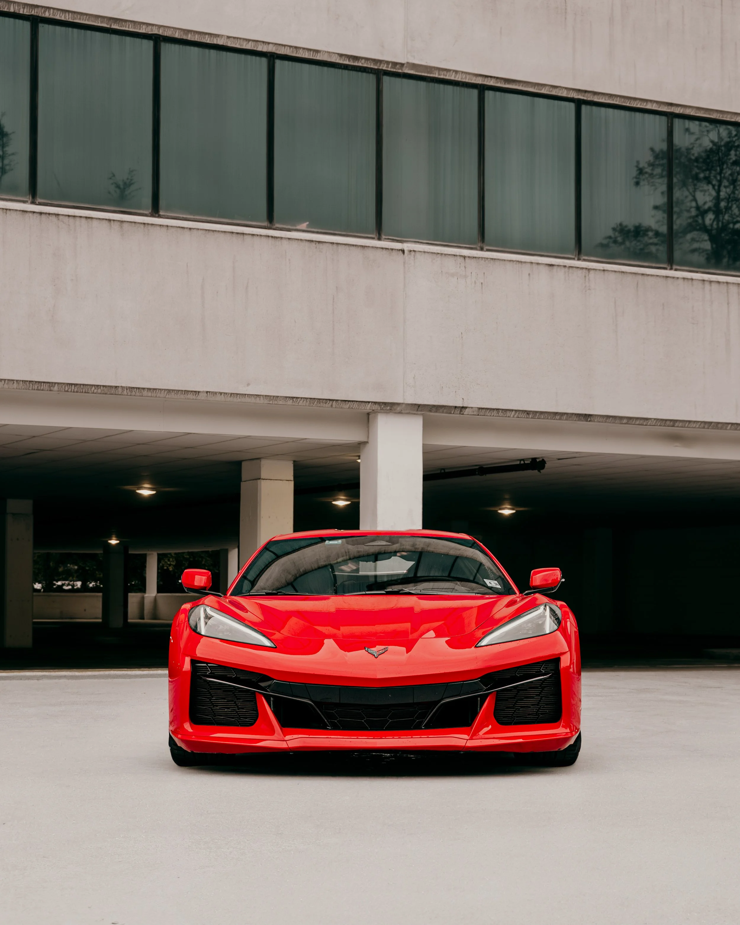 Red sports car parked in front of a building with large glass windows and concrete walls.