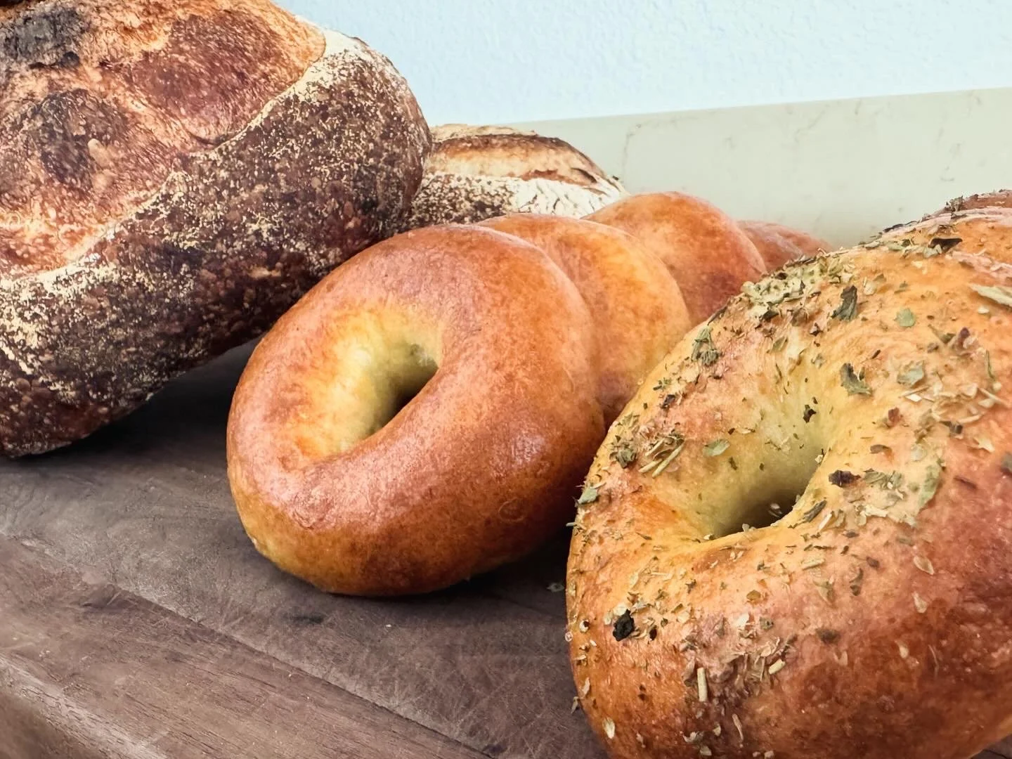 Assorted bagels, including a plain bagel and bagels with sesame and herbs, on a wooden surface.