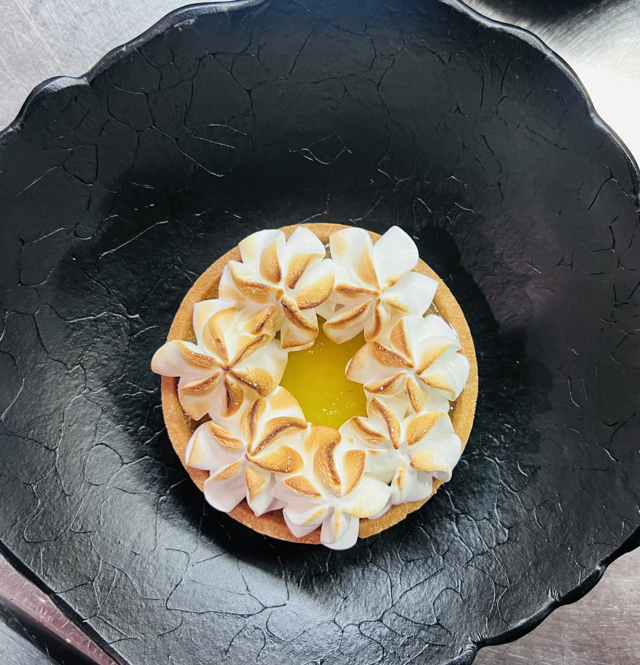 A dessert tart topped with toasted marshmallows on a black textured plate.