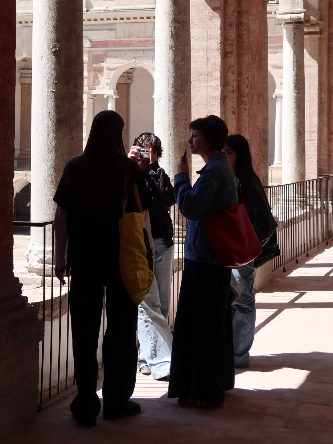 Quattro persone stanno facendo una foto o un selfie in un sito archeologico con colonne di pietra e archi in background, probabilmente un monumento storico o un tempio.
