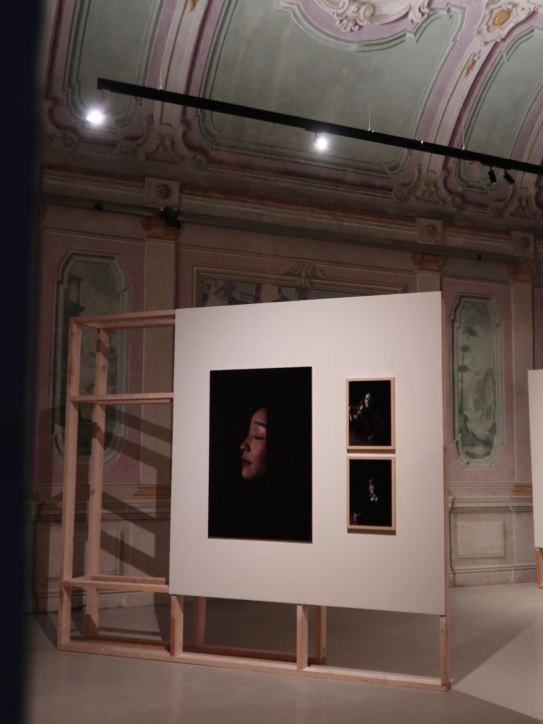 Mostra d'arte con fotografie di ritratti di donne in un ambiente con pareti decorate in stile barocco.