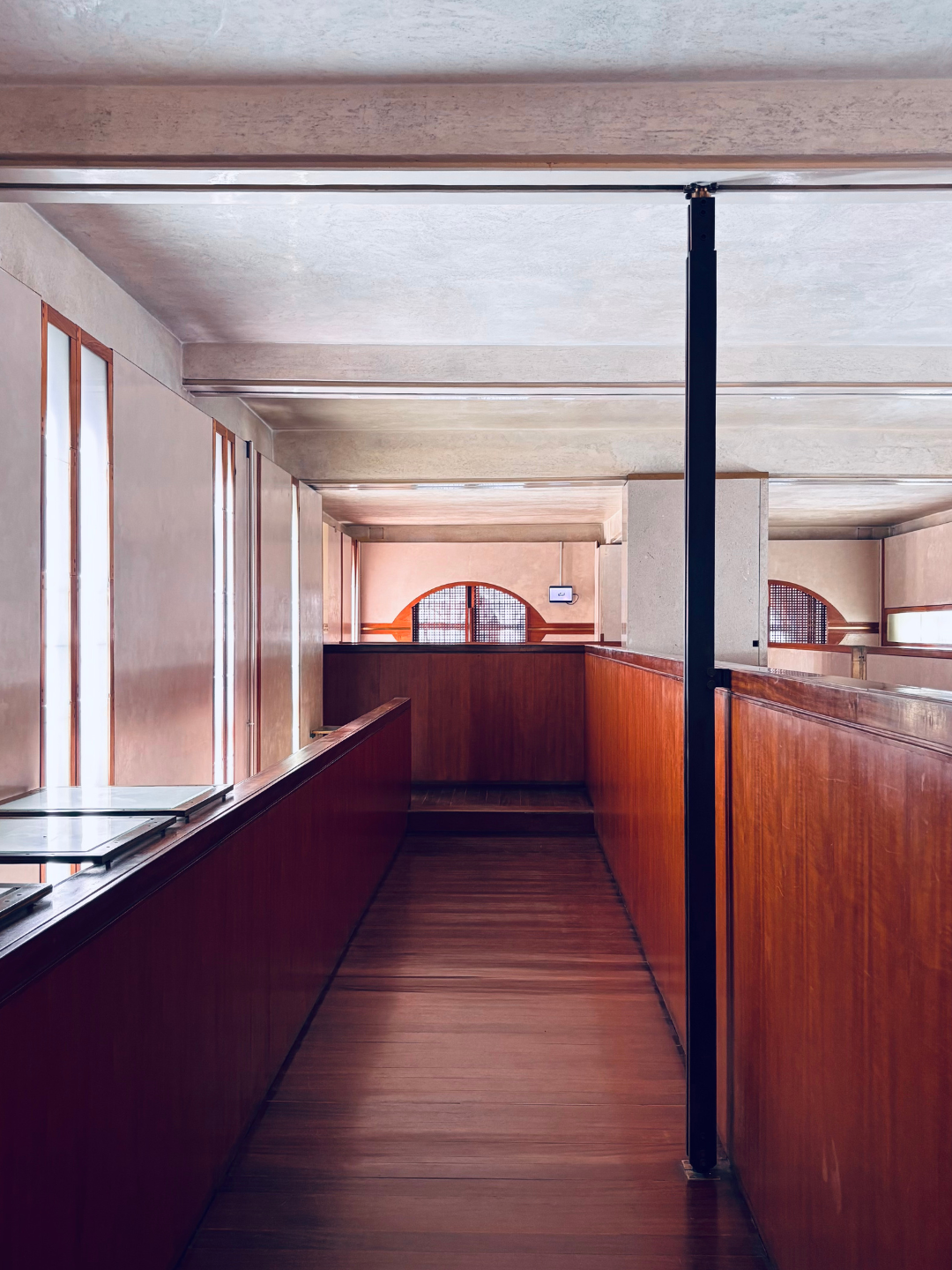 Interno di un edificio con pareti di legno e finestre ad arco, pavimenti in legno chiaro, una colonnina nera al centro.