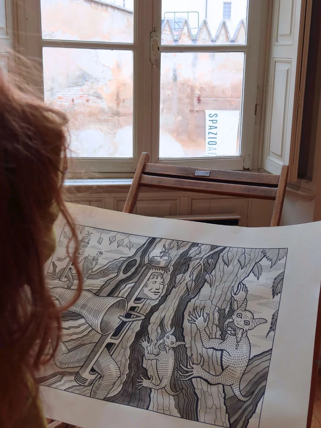 Studio d'atmosfera e narrazione visiva all'interno dello spazio espositivo: prospettiva laterale di una visitatrice che analizza un disegno su carta a Mantova.