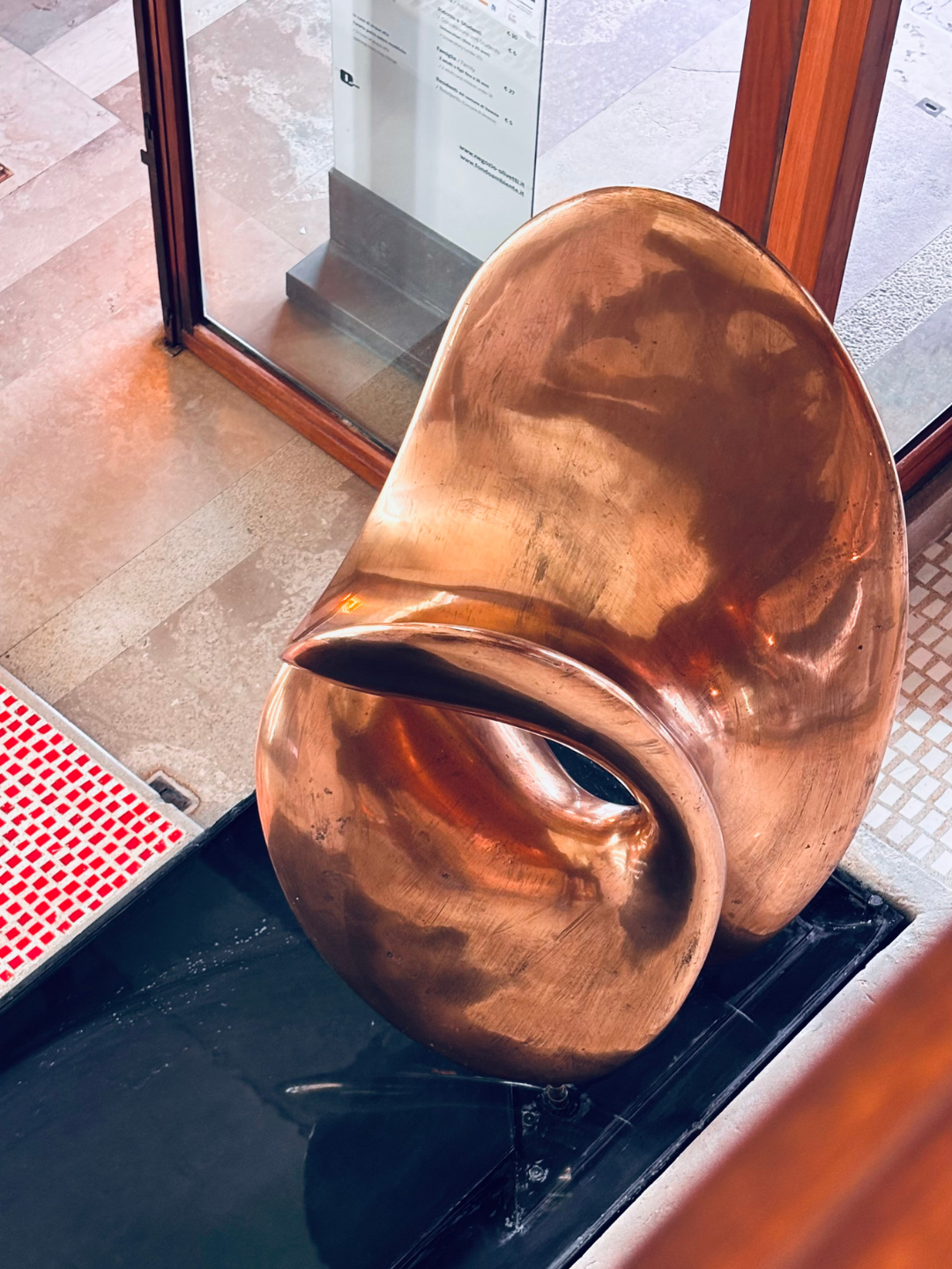 Scultura moderna in ottone e acqua, situata all'ingresso di un edificio.