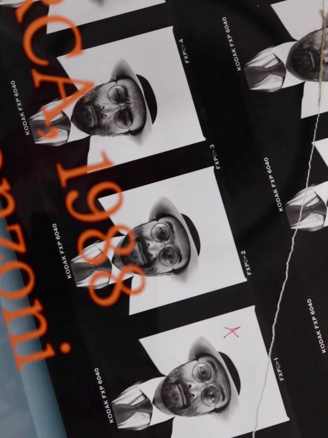 Set di quattro strisce di pellicola fotografica in bianco e nero con ritratti di uomo con barba, occhiali e cappello, vestito con giacca e cravatta, sopra una superficie nera.