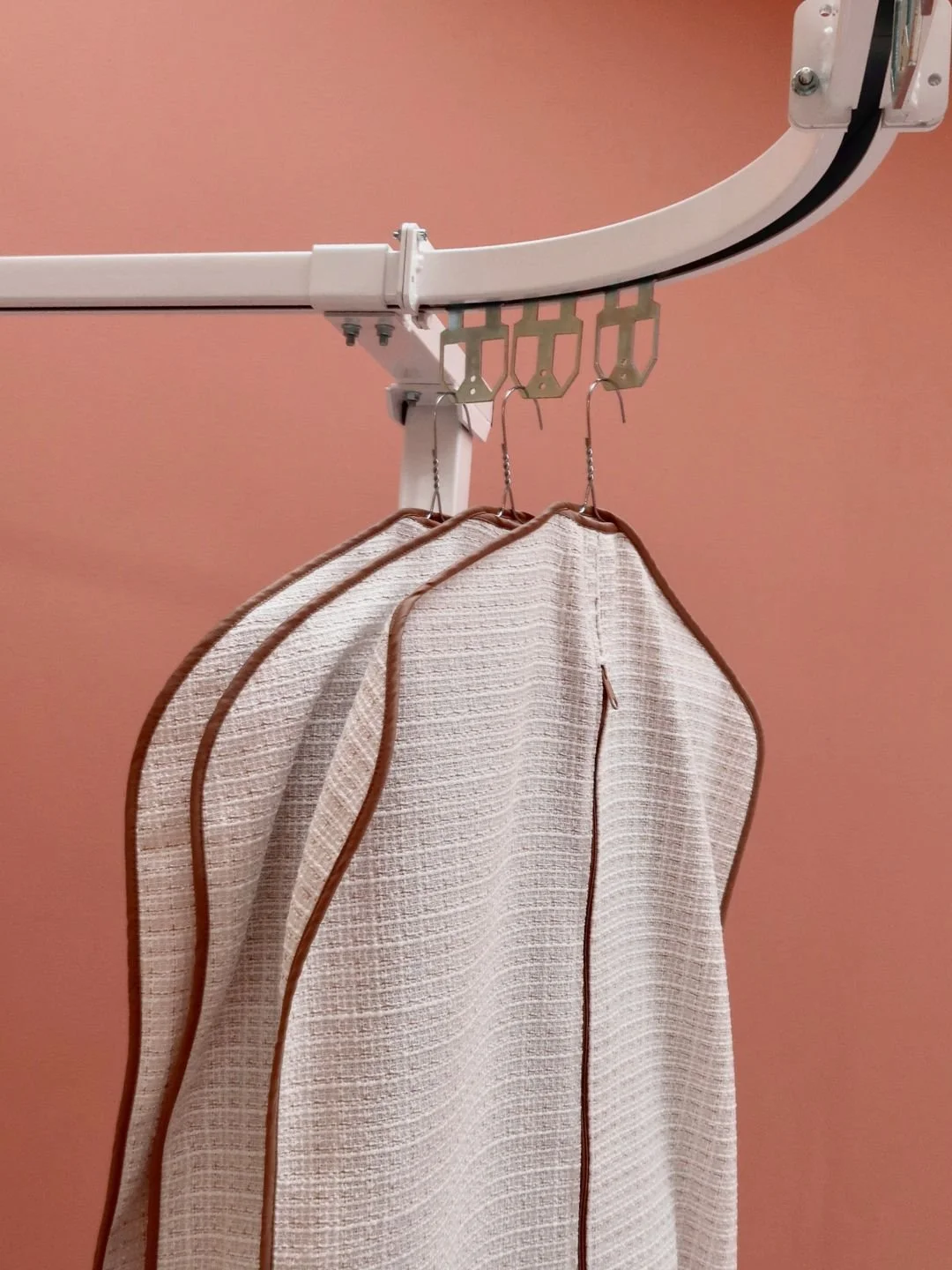 Asciugamani beige con bordature marroni appesi a ganci su una barra di un bagno con pareti rosa.