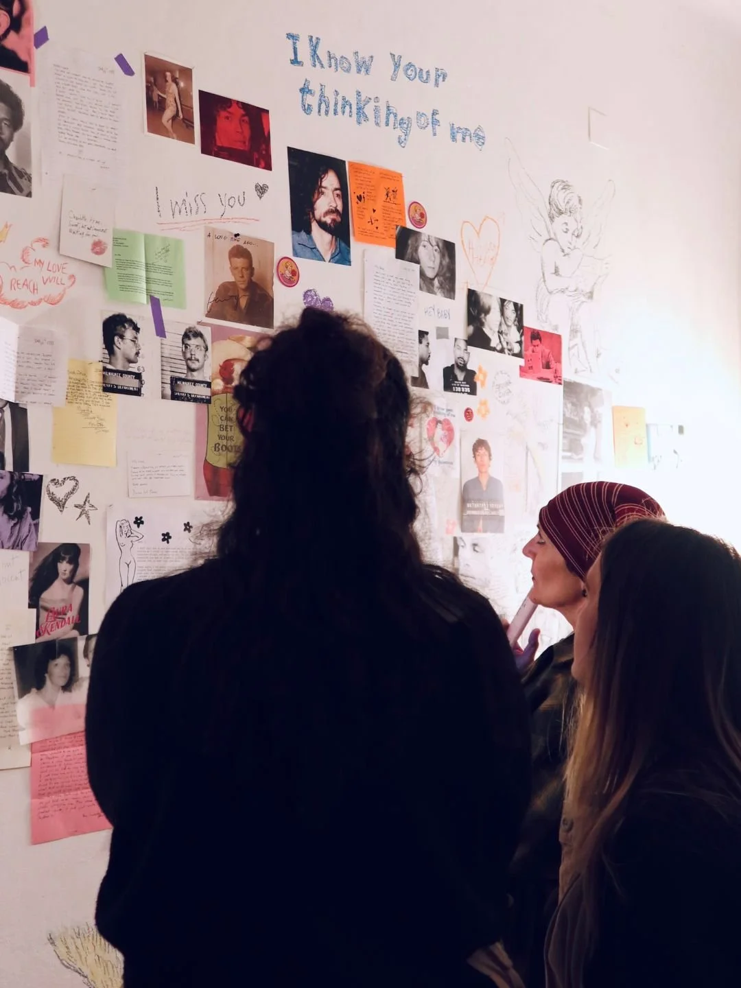 Documentazione visiva dell'installazione artistica Hungry Heart a Mantova. Visitatori di spalle osservano il collage e la scrittura d'artista sulla parete espositiva.