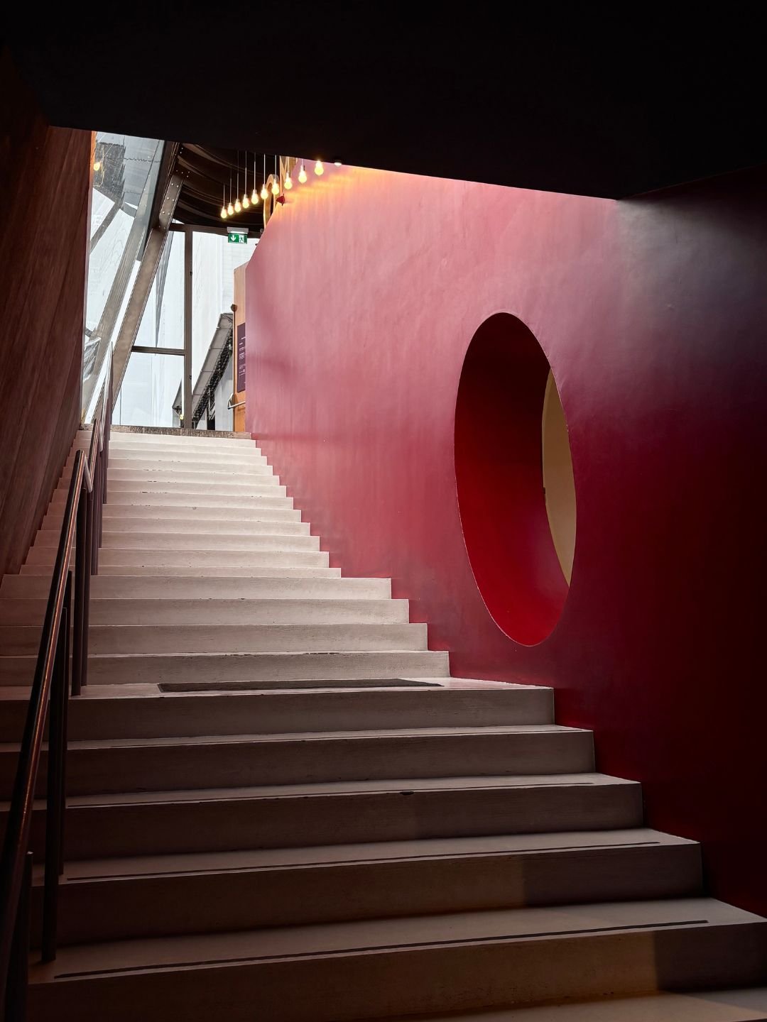 Scala in un edificio moderno con pareti rosse e decorazioni di luci appese.