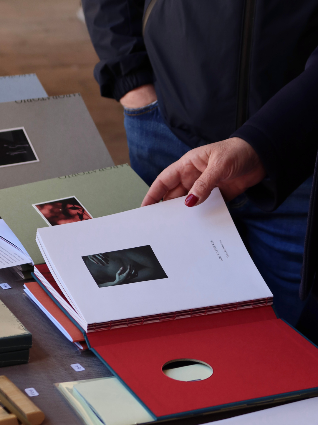 Persona che sfoglia un catalogo con immagini e testo, con altri cataloghi e materiali su un tavolo