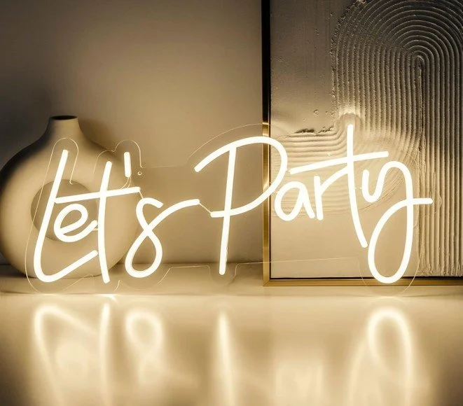 A neon sign that says "Let's Party" is displayed on a light-colored surface, with a white decorative vase and framed artwork in the background.