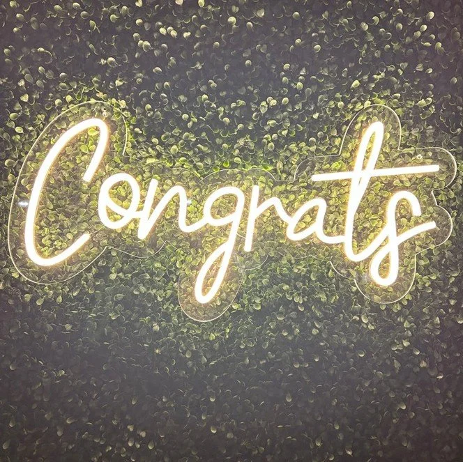 Neon sign that reads 'Congrats' in front of a leafy green background.