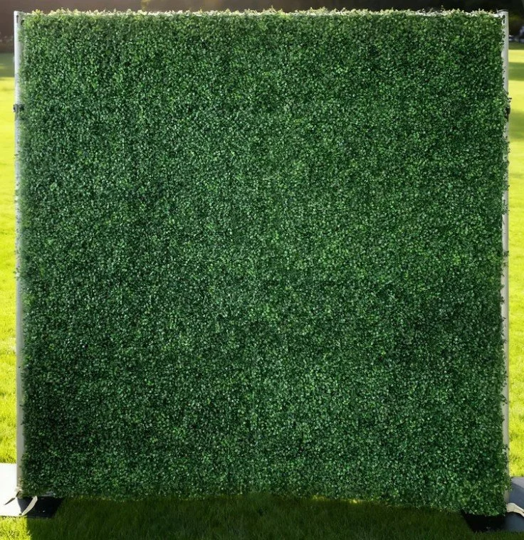 Large artificial green hedge wall outdoors with grass in the background.