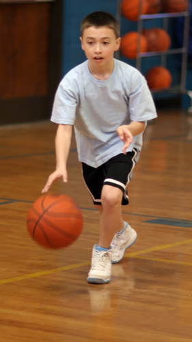 Young boy playing basketball on an indoor court, dribbling the ball.