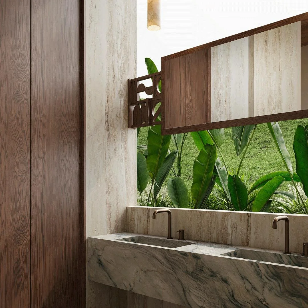 Modern tropical bathroom with a floating stone double vanity, integrated sinks, bronze fixtures, travertine walls, custom wood mirrors, and views of lush greenery. A refined, nature-inspired interior blending luxury and organic materials.