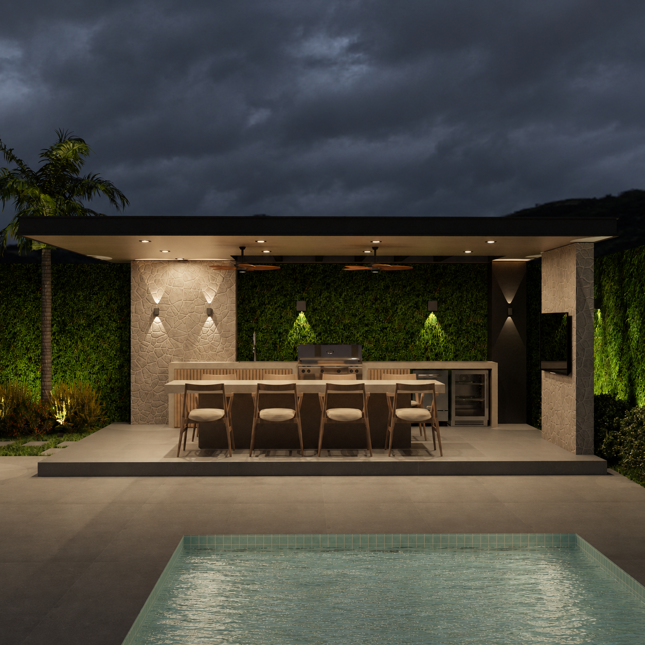 Modern outdoor kitchen area with barstools, built-in grill, and a television, illuminated by wall and ceiling lights, with a swimming pool in the foreground, under a cloudy sky at dusk.