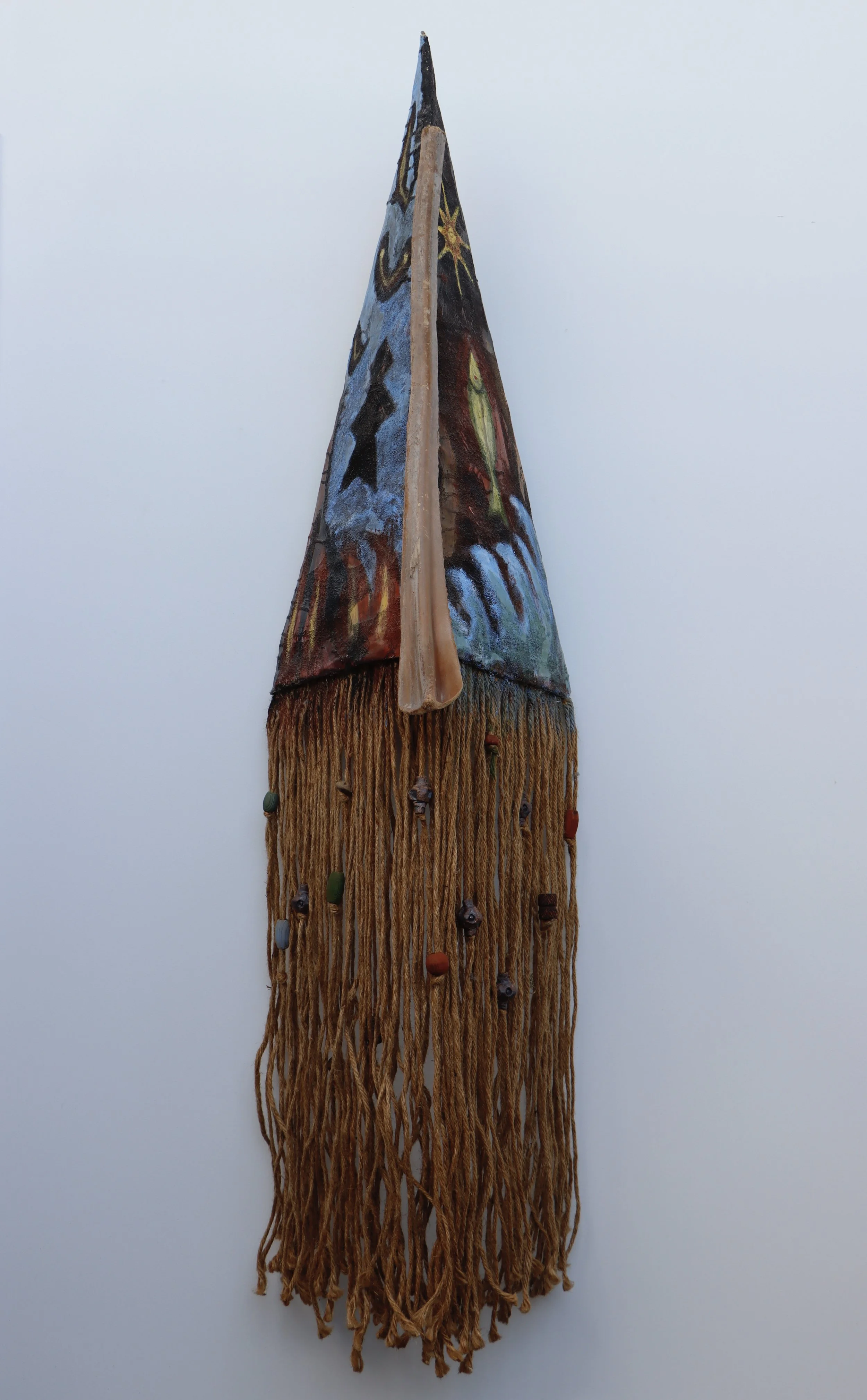 A decorative hanging piece featuring a painted animal face on fabric, with fringes and small beads hanging at the bottom.